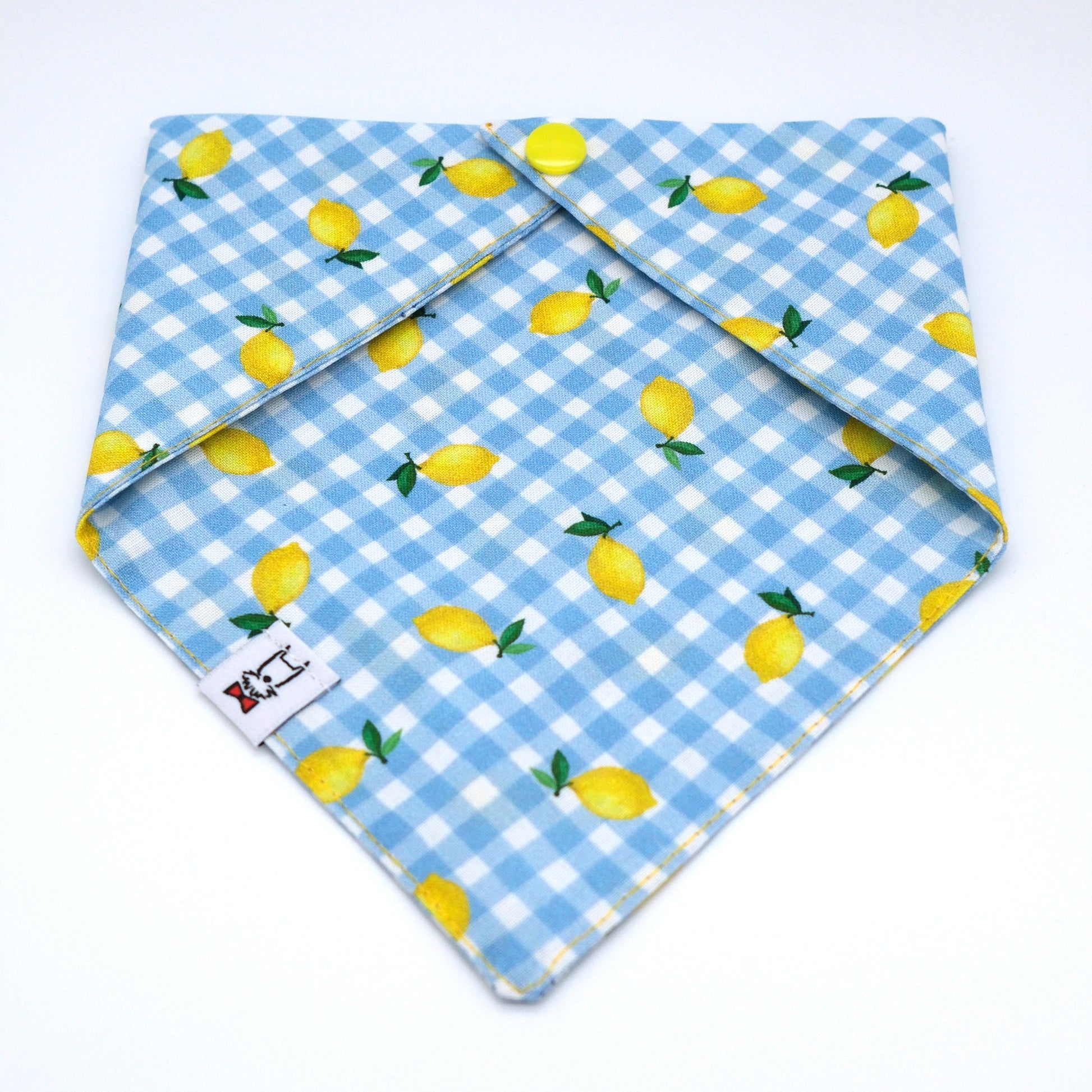 A light blue and white gingham bandana dog collar with a yellow lemon print, folded to show its interior and a small white brand tag.
